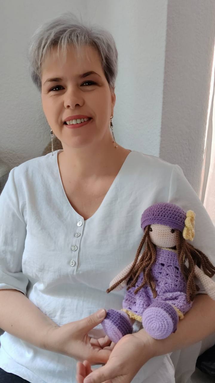 Profe Anita sonriendo con una muñeca amigurumi lila en los brazos
